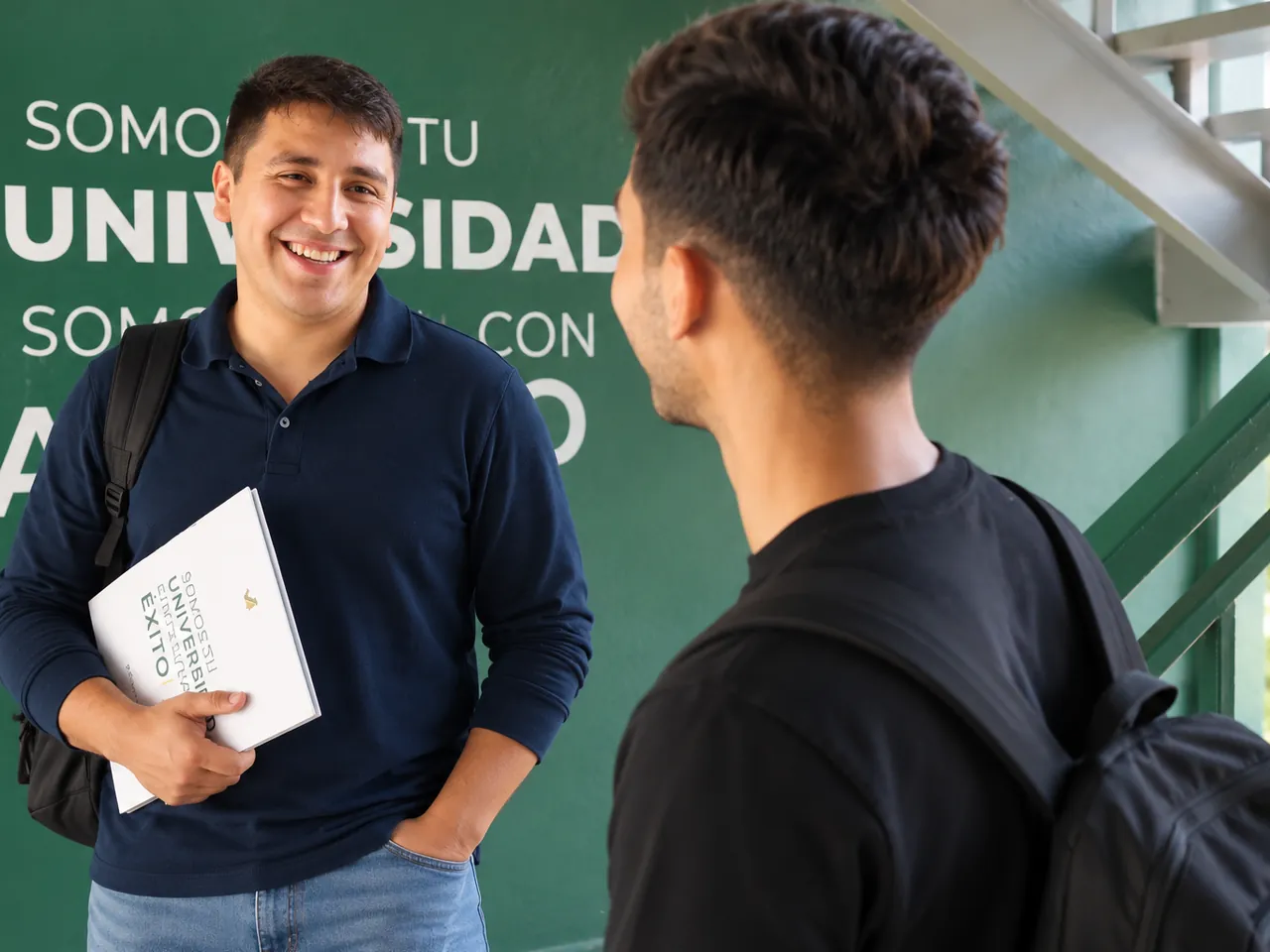 Alumno sonriente en el campus con su carpeta de la universidad